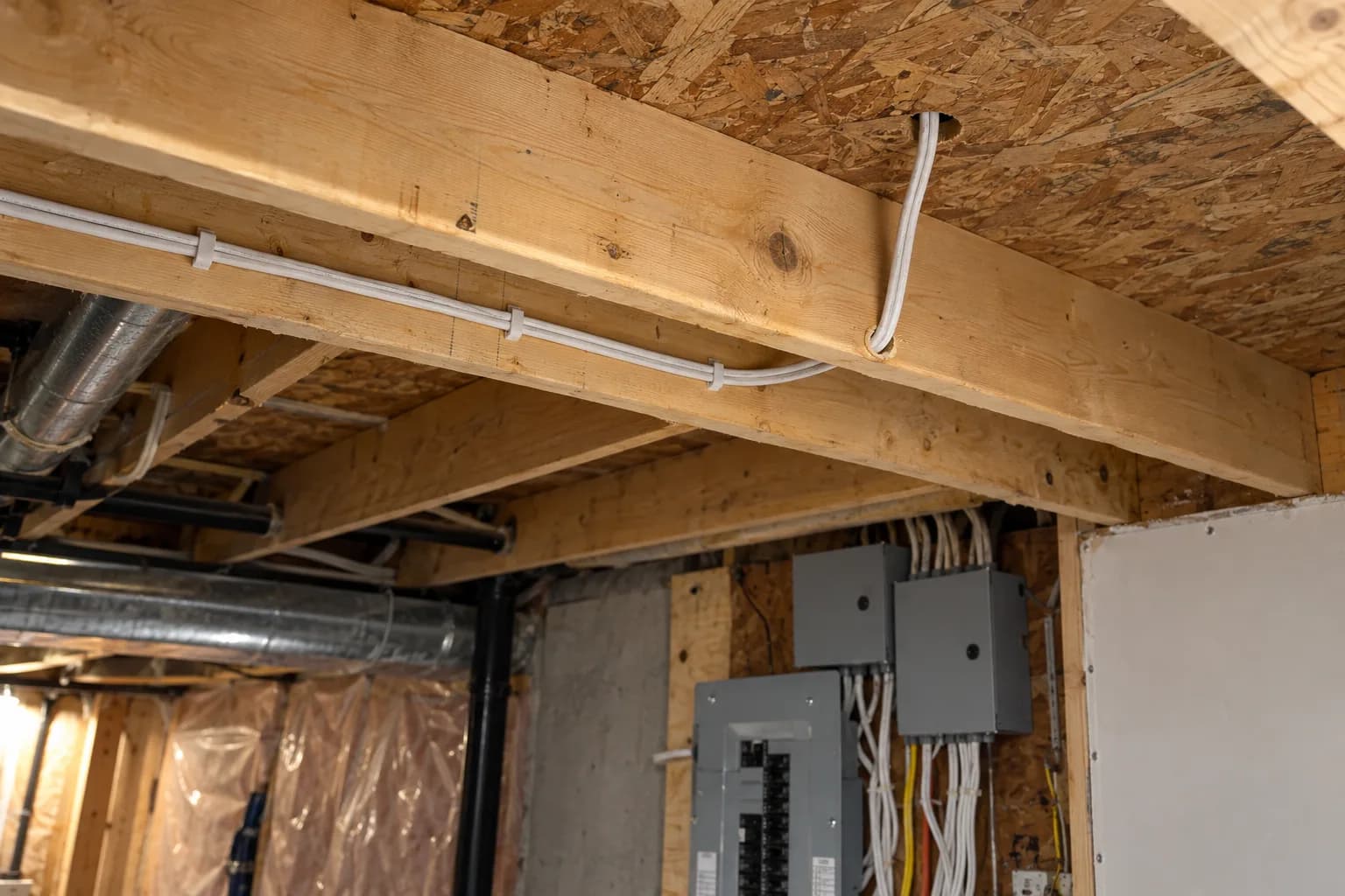 Unfinished basement ceiling with a new white cable run along the joists and up through the floor to the room above