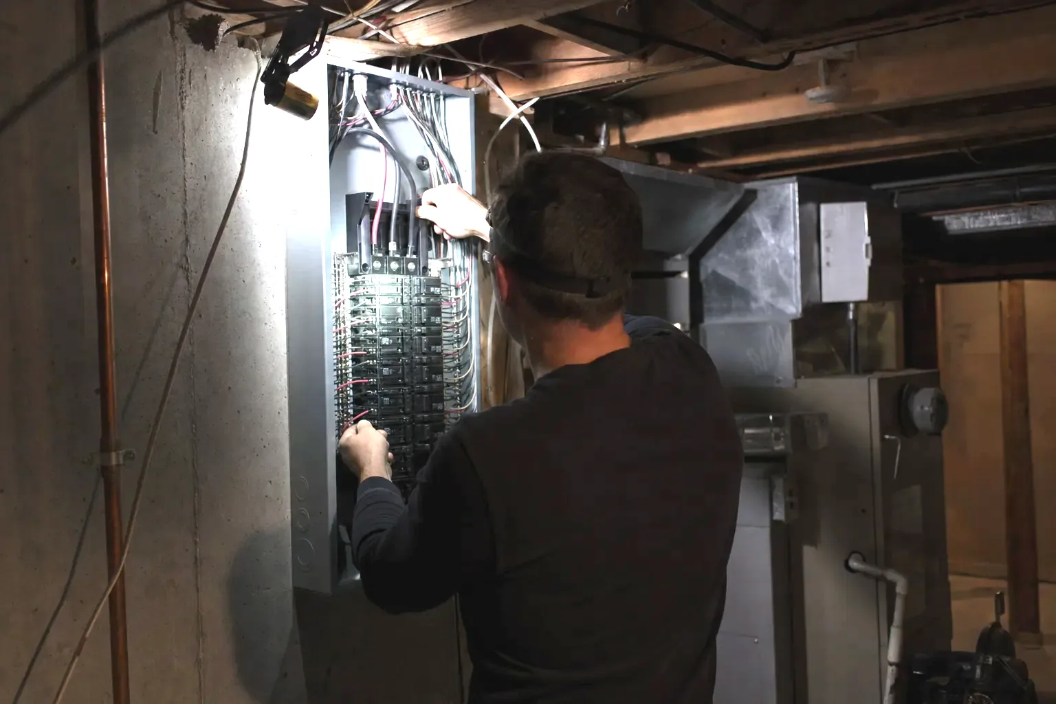 Electrician working inside an open 200-amp panel by headlamp during a night call in a Mississauga basement