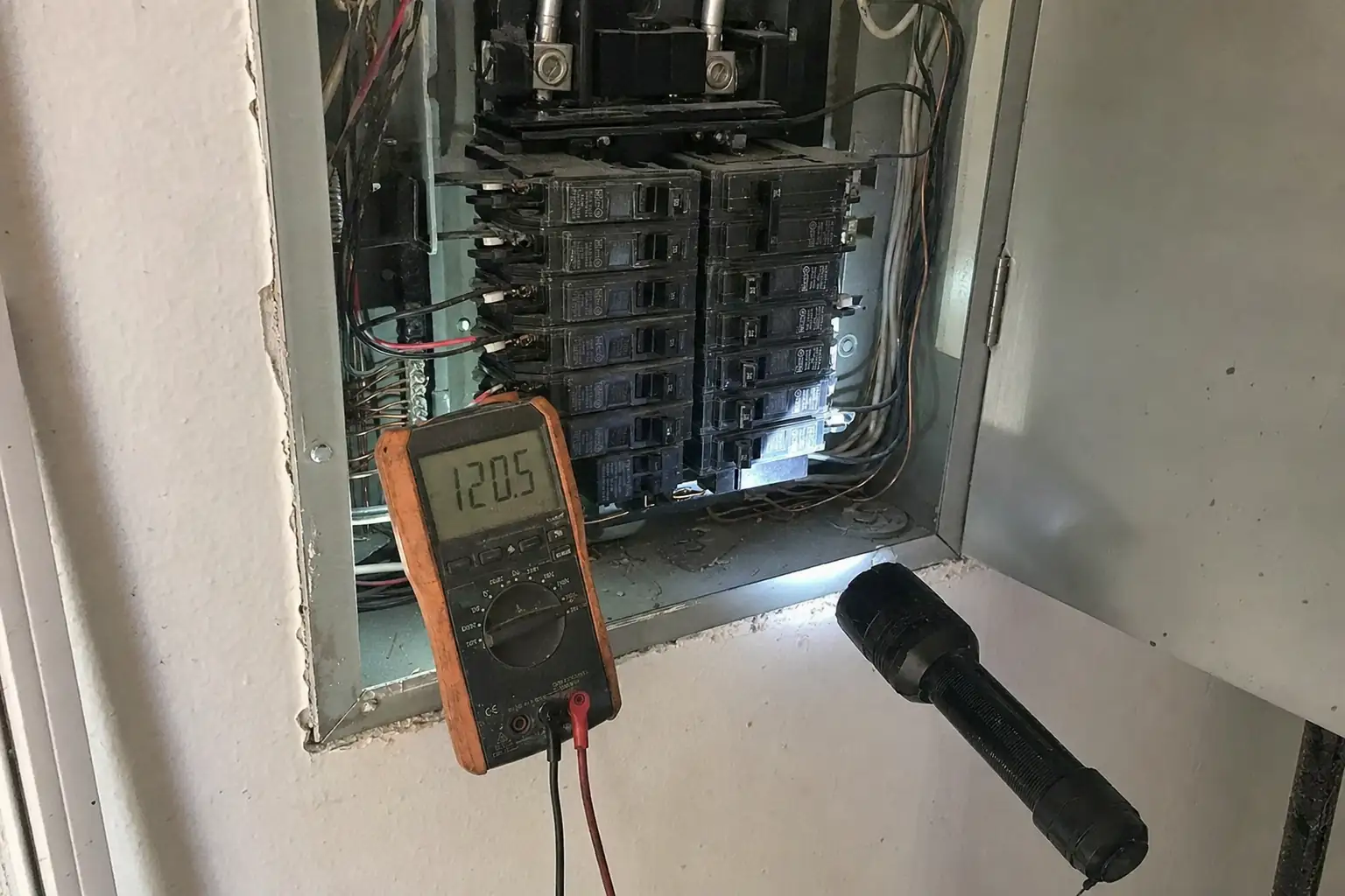 Multimeter testing an open electrical panel during the $49 assessment